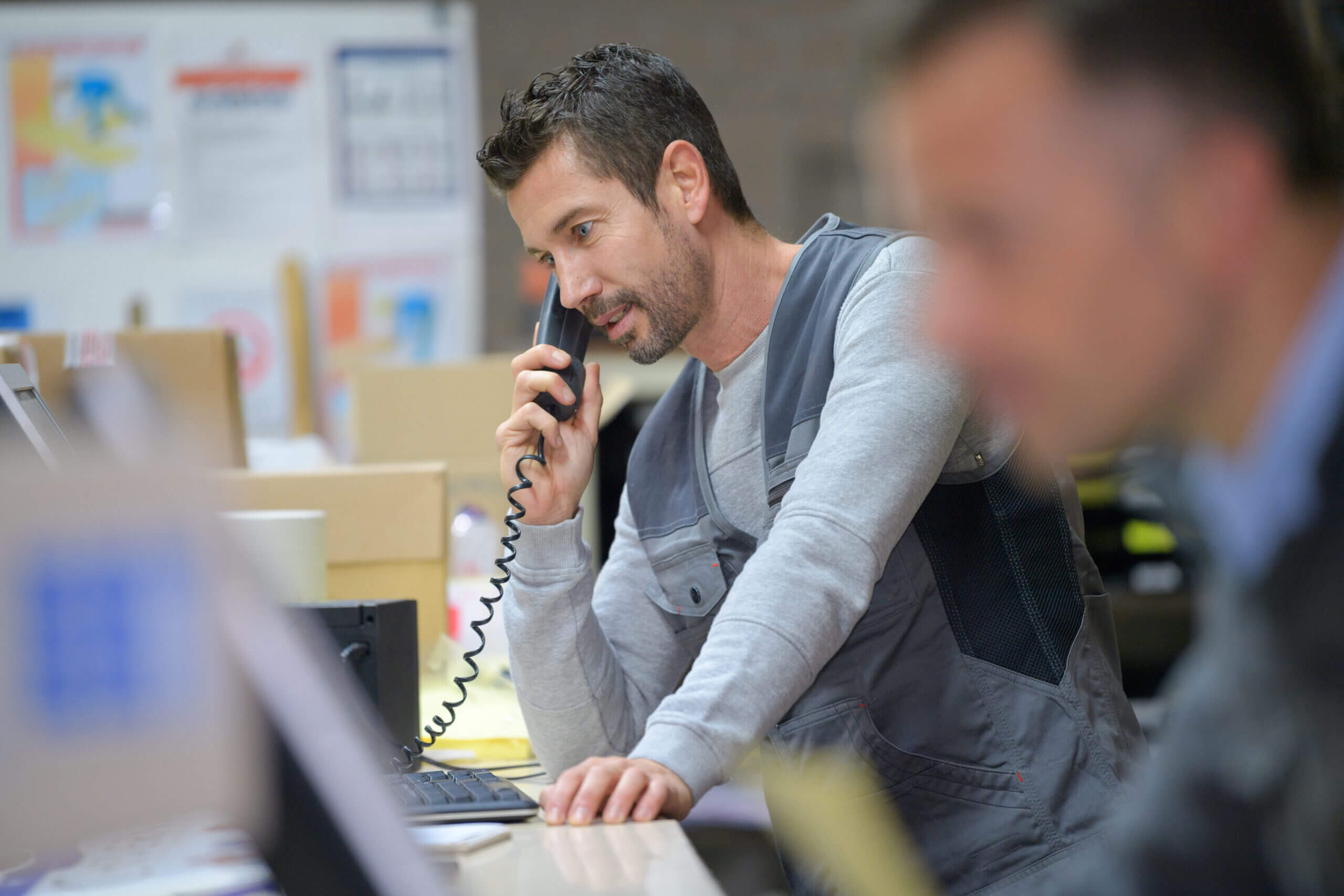A business man talking to a customer on a hosted phone while looking at a computer.